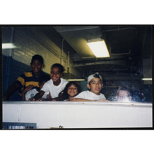 Five Boys & Girls Club members smiling for the camera from the other side of a window