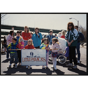 A boy and three girls holding the "Little Patriots Child Care Center" sign while several adults stand behind them at the Boys and Girls Clubs of Boston 100th Anniversary Celebration Parade