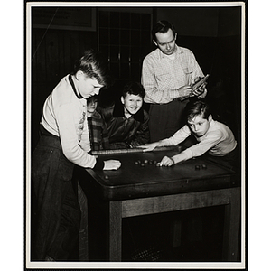 Two boys play a table game as two other boys look on and a man keeps score