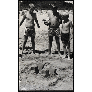 Three boys look at a sand castle on a beach