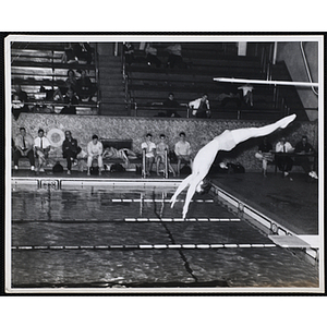 A teenage boy executes a dive in a natatorium pool as a spectators look on