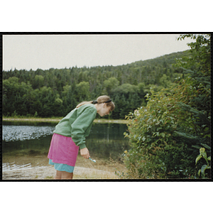 A girl brushes her teeth on the shore of a pond