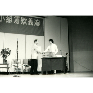 Two men shake hands on stage during a skit for the Chinatown Task Force Fundraiser