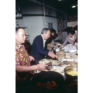 Men and women serve themselves around a buffet table