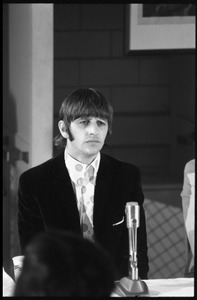 Ringo Starr seated in front of a microphone at a table, during a Beatles press conference