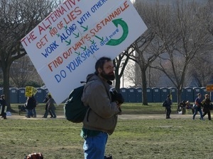Protester on the National Mall marching against the War in Iraq, carrying a sign advocating for sustainability
