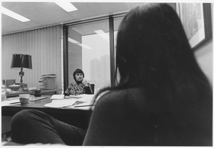Jean R. Leppaluoto sitting indoors, behind desk, talking to a student