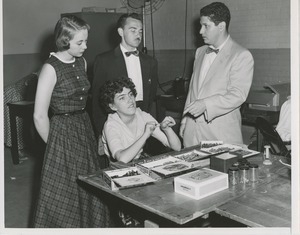 Woman performing assembly tasks for three onlookers