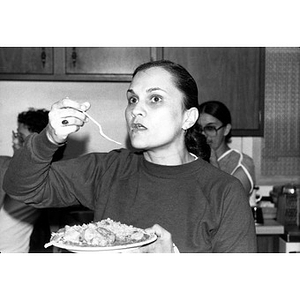 Young woman pauses with a fork halfway to her mouth during a community gathering.