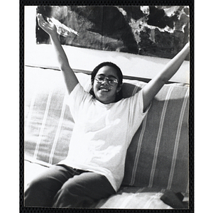 A girl, wearing glasses, raises her arms in the air while sitting on a couch at the Charlestown Boys & Girls Club