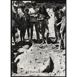 A group of girls gather around a sand castle on a beach