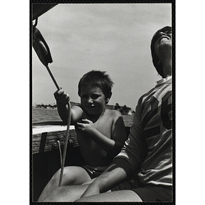 A boy sits next to a teenage boy on the deck of sailboat in Boston Harbor