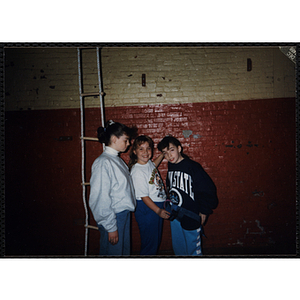 Three girls stand next to a ladder in a gymnasium