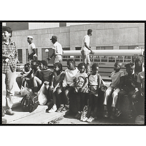 A group of children sit by a staircase in front of a school bus