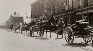 Street-level view of soldiers and horse-drawn artillery marching through a town