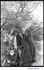 Peter Simon seated on a motorcycle, with Usha (Cathy Brown, right) and two other admiring women standing around him