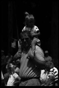 Girl waving a small American flag, sitting on her father's shoulders watching the Chesterfield's Fourth of July parade
