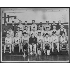 Group portrait of track team and coaches with trophies on bleachers