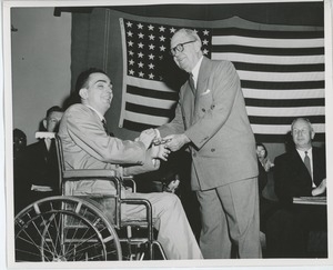 Jeremiah Milbank, Sr. shaking hands with young man in wheelchair at graduation exercises