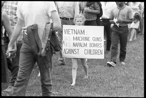 Young girl marching with protesters, carrying sign reading 'Vietnam: US machine guns, US napalm bombs, against children'