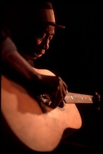 Mississippi John Hurt: studio portrait, seated, playing guitar