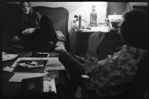 Judy Collins, seated on a bed at the Beverley Hills Hotel, talking with an unidentified man