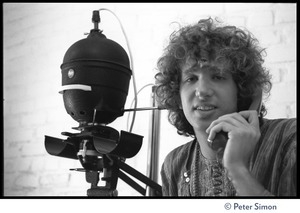 Peter Simon seated in a darkroom next to an enlarger, talking on the telephone