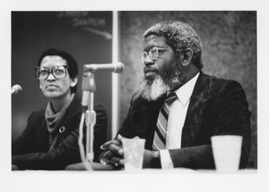 Johnnetta B. Cole sitting indoors behind microphone, next to an unidentified man