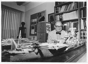 Hugh F. Bell sitting indoors behind the model of a ship