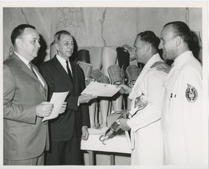 James Burrows presents a certificate of completion of training to a 1964 Prosthetics and Orthotics training graduate while two other men look on