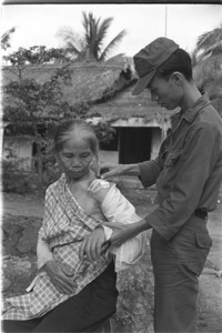 Army doctor dressing wound of an old woman hurt by shrapnel during Vietcong attack; Luong Hoa Village.