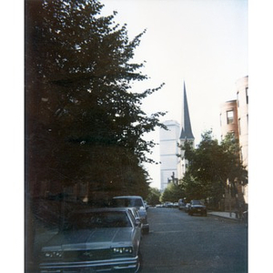 Street in the Villa Victoria neighborhood, with a church spire and a skyscraper in the distance.