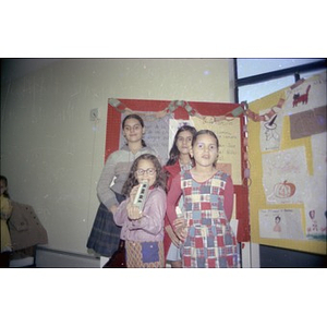 Four girls standing in front of a display of children's drawings and stories.
