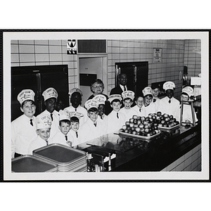 Members of the Tom Pappas Chefs' Club stand for a group shot with Chefs' Club committee member Mary A. Sciacca and an unidentified man in a Brandeis University kitchen