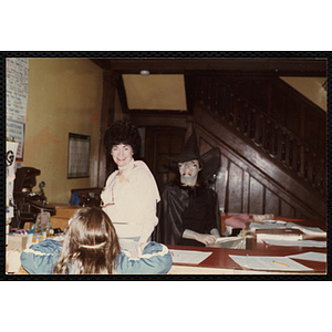 Two women in Halloween costumes stand behind a desk