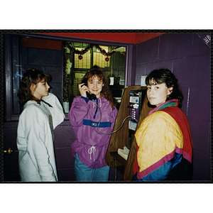 Three girls gather around a pay phone at Roller World during a Tri-Club trip