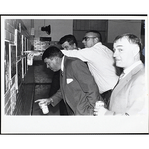 A man looks at the camera while three other men examine photographs on the wall at the South Boston Boys & Girls Club Alumni Party