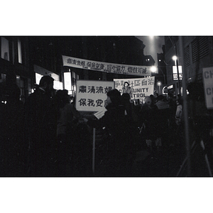 Silhouette of a crowd listening to a woman speak at an evening demonstration led by residents of Chinatown to take back their community from the Combat Zone, the red-light district in Boston