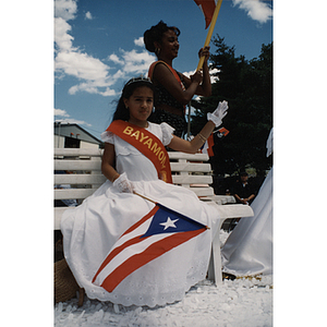 A girl representing the municipality of Bayamon waves from a parade float at the Festival Puertorriqueño