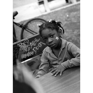 Little girl sitting at a table outside with a star painted on the side of her face.