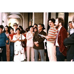 Jorge Hernandez addressing neighborhood residents from outside in front of the laundromat under the arcade.