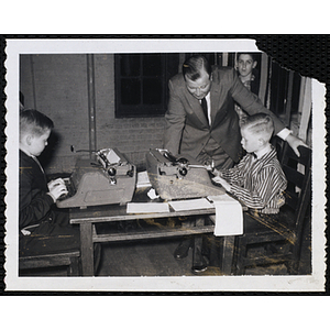 Two boys sitting at typewriters while a man looks on at the Boys' Club Awards Night Exhibit