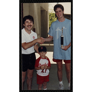 A man with a boy shakes hands with and presents a trophy to a teenage boy during the Battle of Bunker Hill Road Race