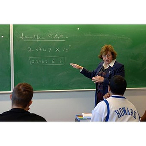 A professor gestures toward the chalkboard during class