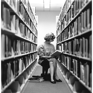 Woman sitting and reading a book in the Snell Library Stacks