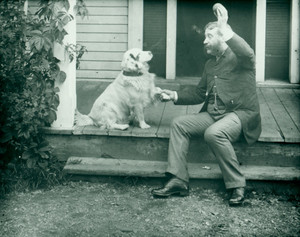 Man seated on a porch playing with a dog, location unknown, 1880s
