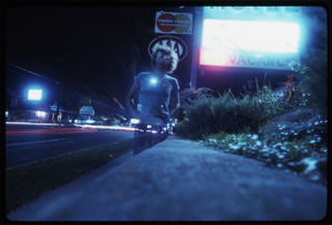 Double exposure of man standing at night by a backlit strip hotel sign