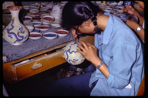 Arts and crafts factory: woman painting ceramics vases with dragon design