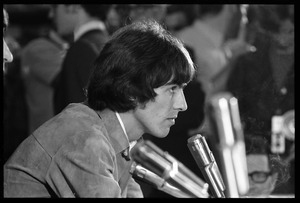 George Harrison in front of a bank of microphones, in profile, during a Beatles press conference