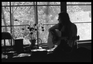 Judy Collins playing guitar while silhouetted against a window in Joni Mitchell's house in Laurel Canyon
